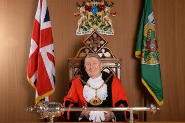The Mayor of Dacorum seated in front of flags and crests