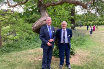 Our long standing trustees, Tony and Mike, standing in front of a tree in the grounds of Buckingham Palace.